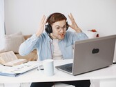 Uomo con le cuffie che alza le mani in segno di frustrazione davanti a un laptop