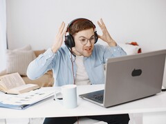 Uomo con le cuffie che alza le mani in segno di frustrazione davanti a un laptop