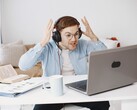Uomo con le cuffie che alza le mani in segno di frustrazione davanti a un laptop