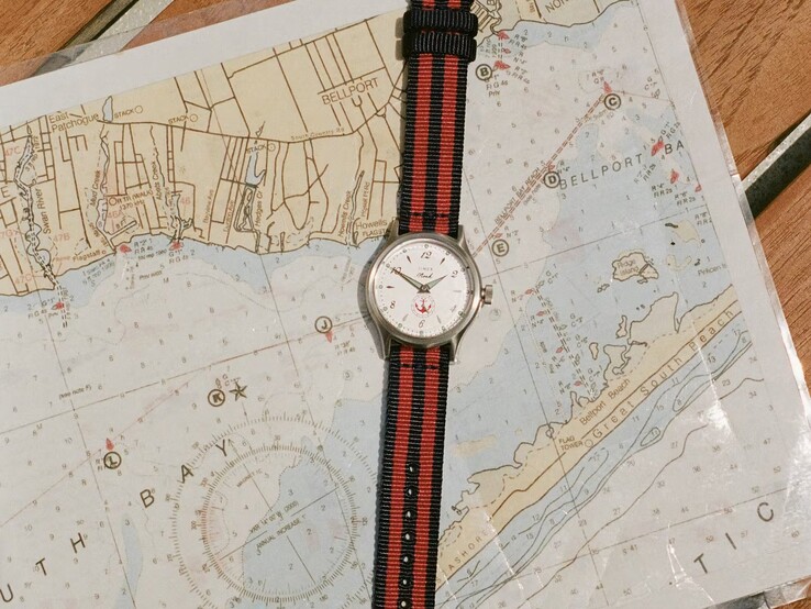 Orologio Noah x Timex MK1 Anchor con cinturino in tessuto a strisce blu navy e rosse appoggiato su una carta nautica.