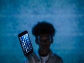 Smartphone sospeso con codice sullo schermo davanti a uno sfondo blu, con una persona sfocata dietro