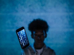 Smartphone sospeso con codice sullo schermo davanti a uno sfondo blu, con una persona sfocata dietro