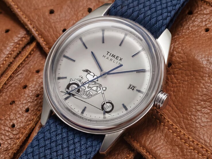 Vista frontale obliqua dell’orologio Peanuts x Timex Marlin Jet Automatic Easy Rider, che mette in risalto il vetro bombato, la cassa in acciaio inossidabile color argento, il quadrante a tema Snoopy e il cinturino in tessuto blu.