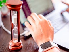 Clessidra accanto a una mano sulla tastiera di un computer portatile