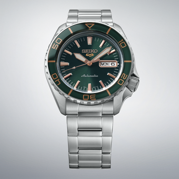 Seiko 5 Sports SKX HDB005 con quadrante verde scuro, lunetta verde abbinata, lancette e indici color oro rosa e bracciale in acciaio inossidabile, mostrato su uno sfondo grigio chiaro.