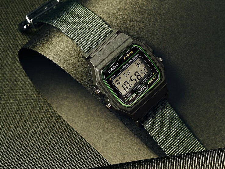 Orologio digitale Casio F-91WF-3A con cassa nera impreziosita da dettagli verdi e cinturino in tessuto intrecciato verde, fotografato su uno sfondo verde scuro con texture.