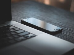 Uno smartphone appoggiato accanto a un laptop aperto su una scrivania buia