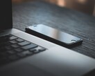 Uno smartphone appoggiato accanto a un laptop aperto su una scrivania buia