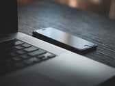 Uno smartphone appoggiato accanto a un laptop aperto su una scrivania buia