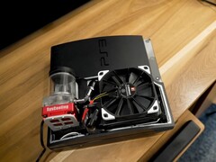PlayStation 3 raffreddata ad acqua personalizzata con una pompa SysCooling rossa e una grande ventola nera montata all'interno del case, posizionata su una scrivania di legno (Fonte immagine: Zac Builds via YouTube)