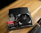 PlayStation 3 raffreddata ad acqua personalizzata con una pompa SysCooling rossa e una grande ventola nera montata all'interno del case, posizionata su una scrivania di legno (Fonte immagine: Zac Builds via YouTube)