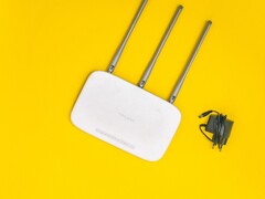 Router Wi-Fi bianco con tre antenne e un alimentatore su sfondo giallo