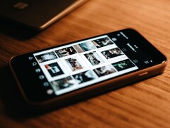 Uno smartphone appoggiato su una scrivania di legno, con il display che mostra una griglia di foto