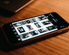 Uno smartphone appoggiato su una scrivania di legno, con il display che mostra una griglia di foto