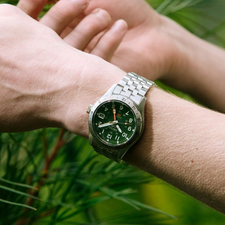 Vista frontale del Seiko 5 Sports Field GMT HDB001, caratterizzato da un quadrante verde, una lunetta fissa in acciaio inossidabile con scala delle 24 ore, una lancetta GMT arancione e un bracciale in acciaio a cinque maglie.