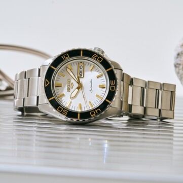 Orologio Seiko 5 Sports SKX HDB004 con quadrante bianco argentato, lunetta girevole nera con marcature color oro, lancette e indici dorati e bracciale in acciaio inossidabile, fotografato di sbieco.