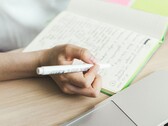 Una persona sta scrivendo appunti su un taccuino accanto a un computer portatile aperto