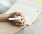 Una persona sta scrivendo appunti su un taccuino accanto a un computer portatile aperto