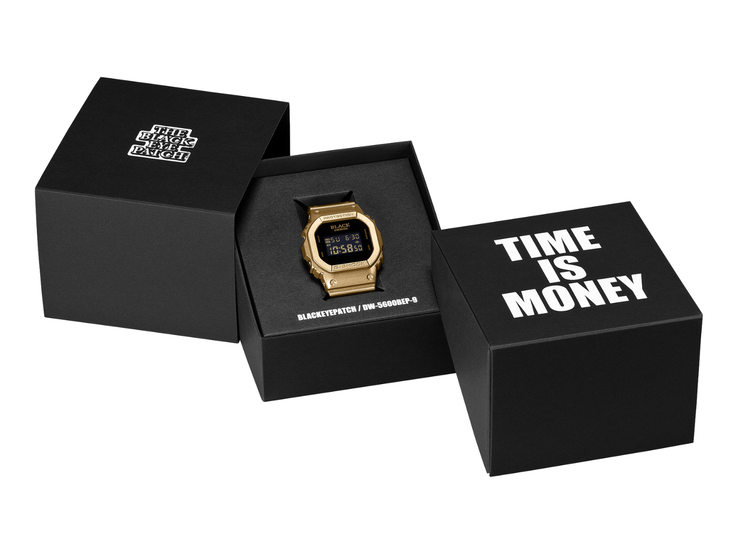Un orologio Casio G-Shock DW-5600BEP-9 dorato con display digitale nero è posizionato tra due scatole da esposizione nere. L’orologio presenta il marchio BlackEyePatch sul quadrante, mentre sulla scatola in primo piano è riportata la scritta «TIME IS MONEY».