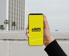 Una mano che regge uno smartphone con la parola «eSIM» scritta a caratteri grandi su uno schermo giallo.