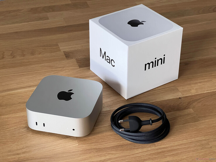Apple Il Mac mini è posizionato accanto alla sua scatola di vendita e al cavo di alimentazione su una superficie di legno della scrivania (Fonte: Notebookcheck)
