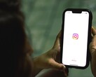 Donna che tiene uno smartphone con entrambe le mani; sul display è visibile la schermata iniziale di Instagram