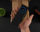 Una persona che tiene in mano la GPU per workstation a basso profilo Intel Arc Pro B50 con un raffreddatore di tipo blower, raffigurata contro la sua scatola di imballaggio. (Fonte: ETA Prime via YouTube)