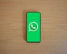 Uno smartphone posato su una scrivania di legno che mostra la schermata iniziale verde di WhatsApp con il relativo logo.