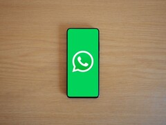 Uno smartphone posato su una scrivania di legno che mostra la schermata iniziale verde di WhatsApp con il relativo logo.