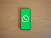 Uno smartphone posato su una scrivania di legno che mostra la schermata iniziale verde di WhatsApp con il relativo logo.